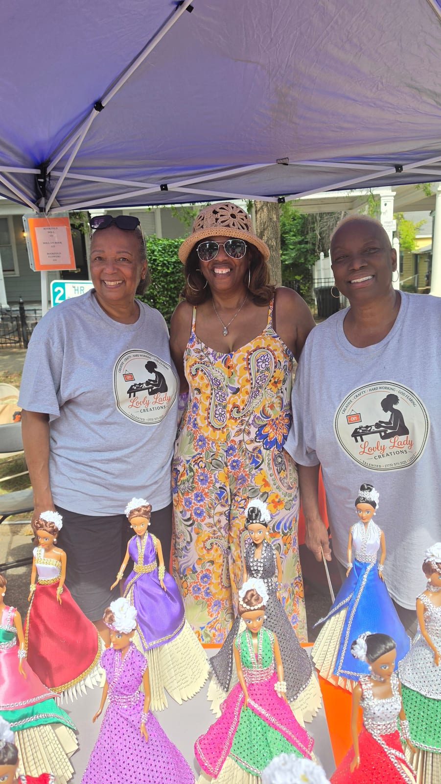 Three community members standing behind a display of handmade dolls